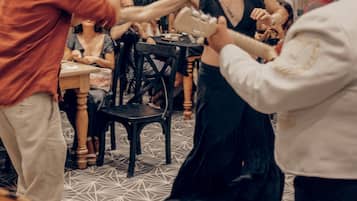 Un grupo de personas bailando en una habitación con piso de diseño geométrico, ventanas amplias y plantas de interior.