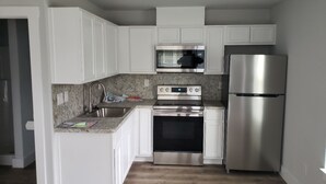 A compact kitchen with white cabinets, a stainless steel stove, a microwave, and a refrigerator.