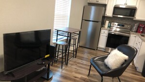 A compact kitchen with a refrigerator, microwave, and stove. There is a dining area with a table and chairs, and a TV on a stand.