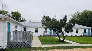 A row of white mobile homes with blue doors and a tree in the center.