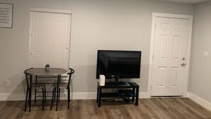 A room with a dining table, chairs, a television on a stand, and two white doors.