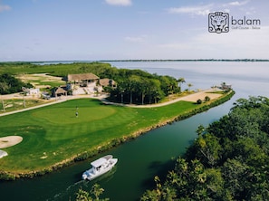A golf course with a water body, a boat, and a building with a thatched roof.