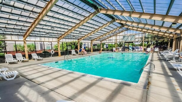 Ein Innenpool mit klarem, blauem Wasser, umgeben von weißen Liegestühlen und einem überdachten Bereich mit einer Metallkonstruktion.