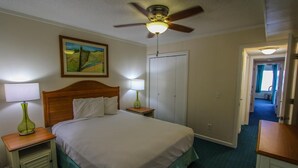 Ein Hotelzimmer mit einem Bett, zwei Nachttischlampen, einem Deckenventilator, einem Bild an der Wand und einer Tür zu einem weiteren Raum.
