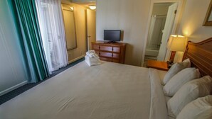 Ein Hotelzimmer mit einem großen Bett, einem Fernseher auf einer Holzkommode, einem Spiegel und einer Lampe.