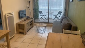 A living room with a sofa, a TV, a wooden table, and a balcony with chairs. - Charming apartment in Sète close to all amenities, secure parking. (Sète)
