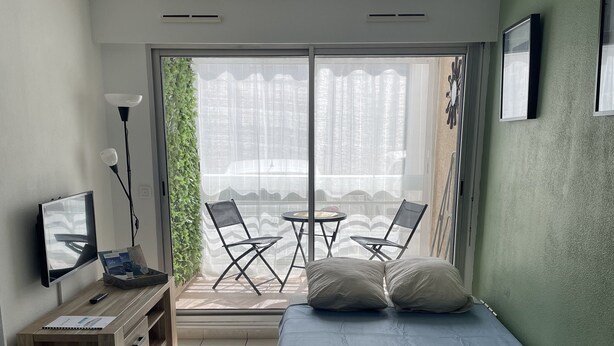 A bedroom with a bed, a desk, a chair, a TV, and a balcony with chairs. - Charming apartment in Sète close to all amenities, secure parking. (Sète)