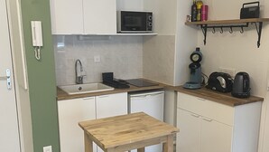 A compact kitchen with white cabinets, a microwave, a coffee maker, and a wooden table. - Charming apartment in Sète close to all amenities, secure parking. (Sète)