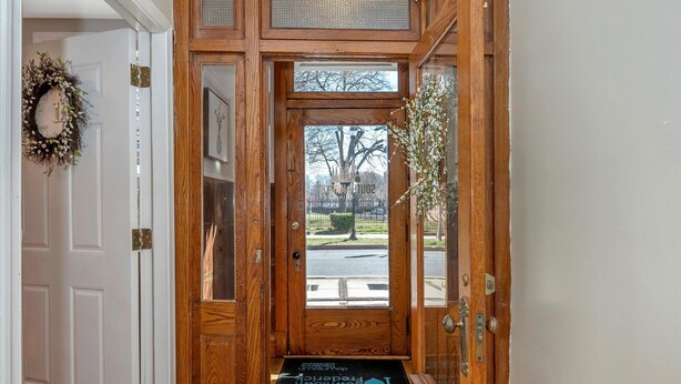 A wooden front door with an exit sign above it, a doormat with a 'Hello' message, and a view of the outside through the glass panels. - Private Ground Level 2BR Condo (Frederick)
