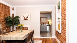 A dining area with a wooden table and chairs, a vase of flowers, and a wall-mounted picture of a cow. - Private Ground Level 2BR Condo (Frederick)