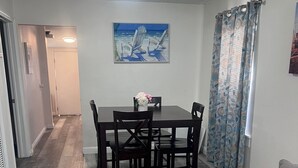 A dining area with a table and chairs, a painting on the wall, and a patterned curtain. - Cozy LBC house (Long Beach)