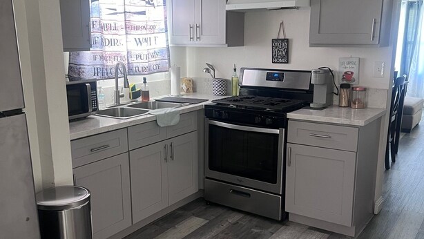 A modern kitchen with grey cabinets, a stainless steel stove, and a microwave. - Cozy LBC house (Long Beach)