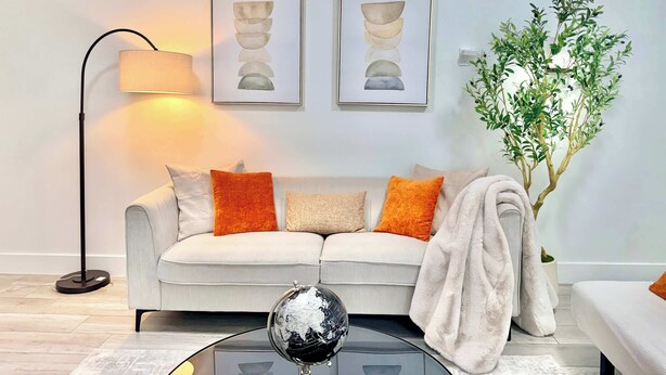 A modern living room with a sofa, a floor lamp, two framed artworks, a globe on a coffee table, and a potted plant. - New Downtown Townhouse, Free Parking Near SkyTrain (Surrey)