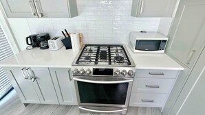 A compact kitchen with a gas stove, microwave, and modern cabinetry. - New Downtown Townhouse, Free Parking Near SkyTrain (Surrey)