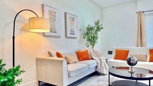 A modern living room with a sofa, a coffee table, a floor lamp, and framed artwork on the wall. - New Downtown Townhouse, Free Parking Near SkyTrain (Surrey)