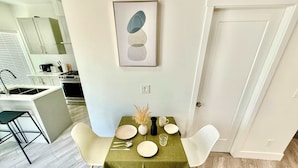 A dining area with a table set for two, a kitchen in the background, and a door to the right. - New Downtown Townhouse, Free Parking Near SkyTrain (Surrey)