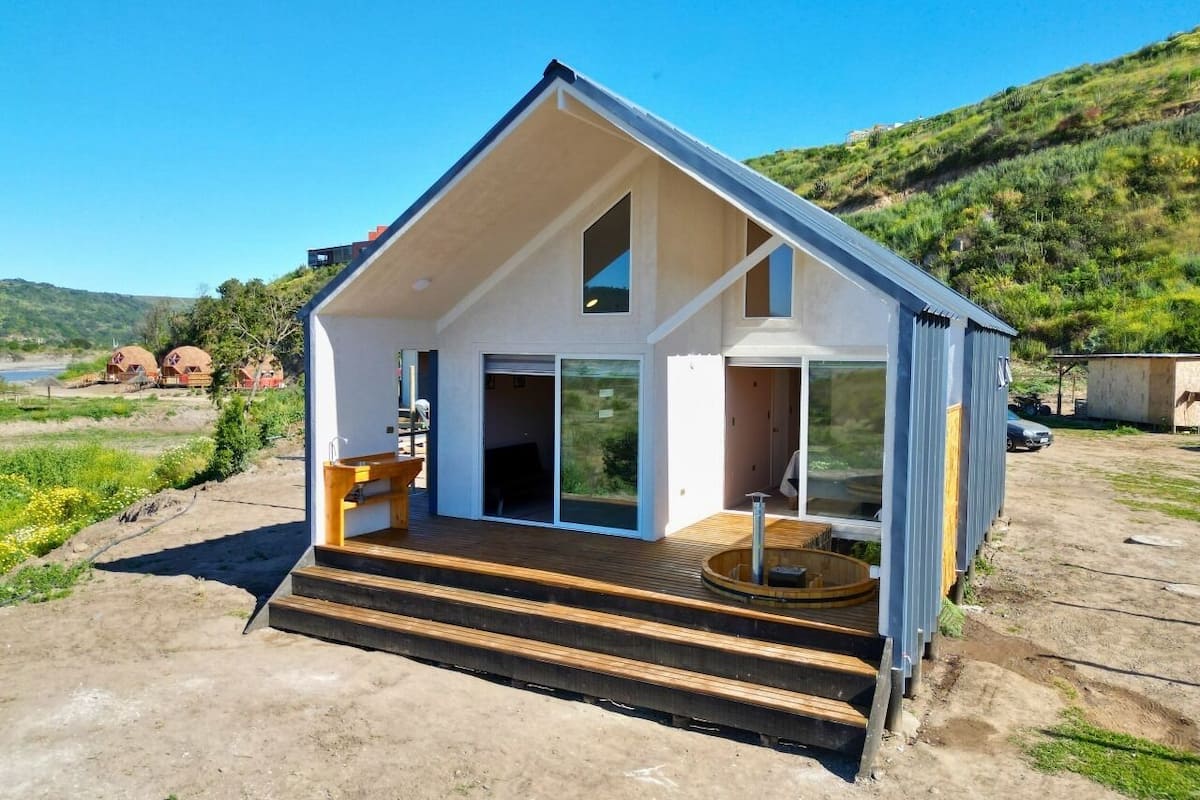 A modern house with a large glass door, a wooden deck, and a view of the surrounding landscape.