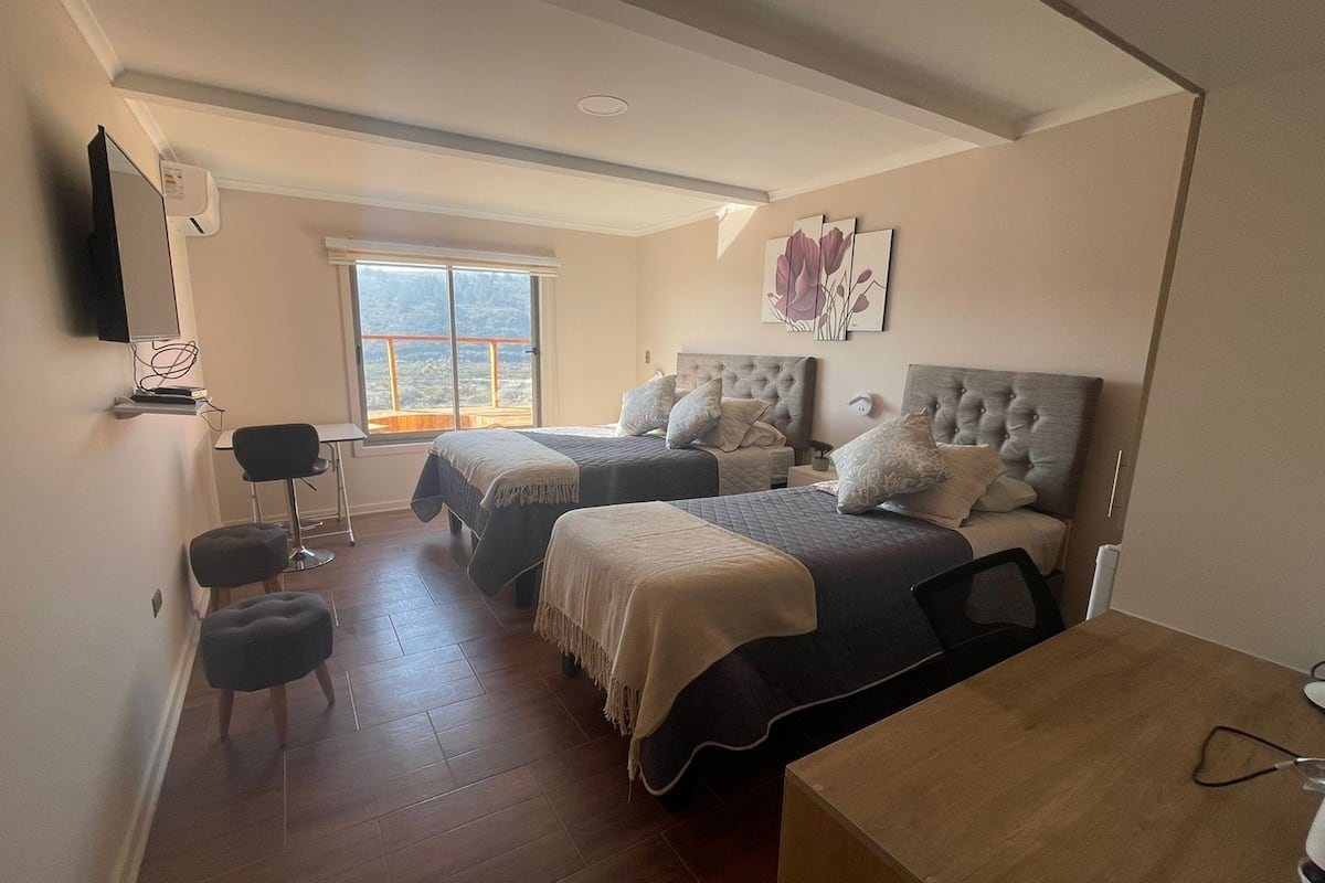 A bedroom with two beds, a desk, a chair, and a window with a view.