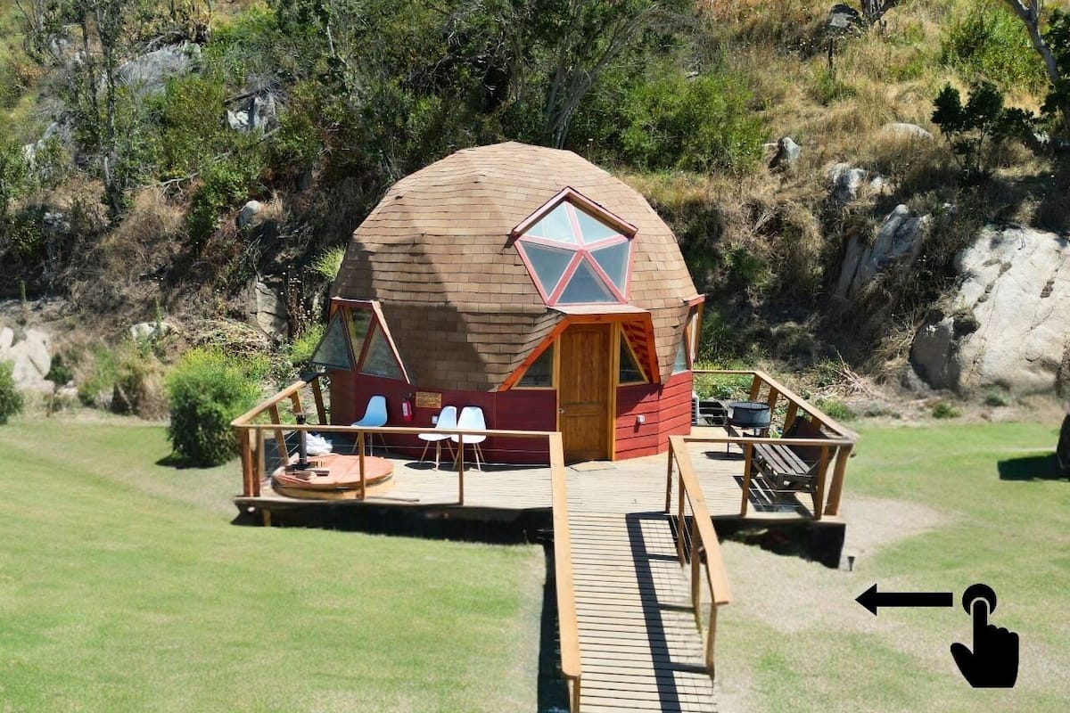 A geodesic dome structure with a wooden deck, seating area, and a small outdoor kitchen.