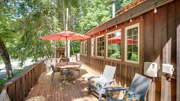 A wooden deck with outdoor furniture, including a table and chairs, and a red umbrella.
