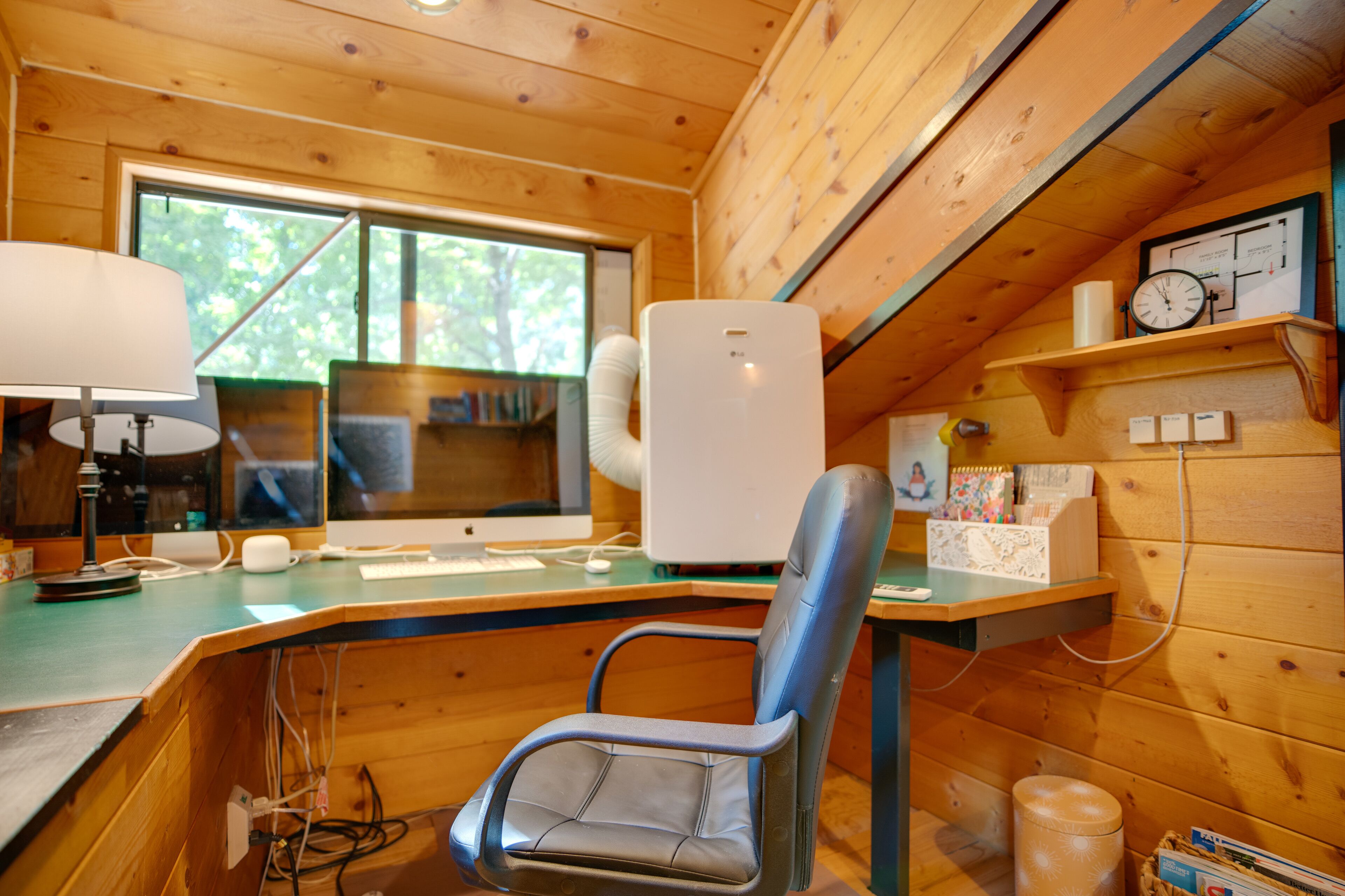 Ein Holzblockhaus-Interieur mit Schreibtisch, Stuhl, Computer, Lampe und Uhr.