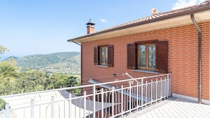 A red brick building with two windows, a balcony with a white railing, and a view of a hilly landscape. - Amazing home in Castellabate with WiFi (Castellabate)
