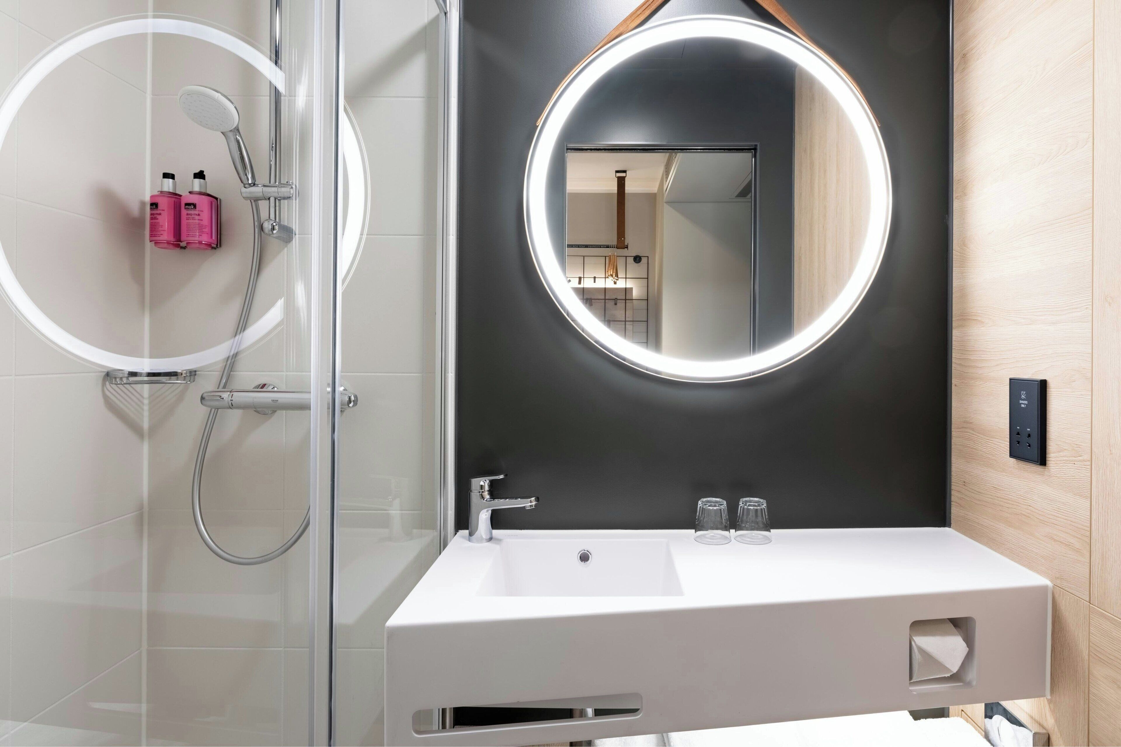 A modern bathroom with a glass-enclosed shower, a white sink with a mirror above it, and a wooden wall panel.