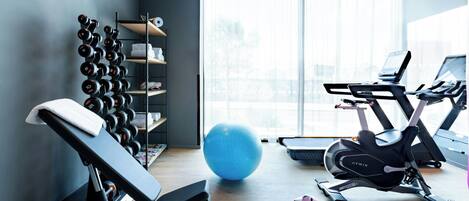 A modern gym with a bench, dumbbells, an exercise ball, treadmills, and a laptop on a desk.