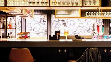 A bar area with a counter, shelves with bottles, a glass of beer, and a graffiti wall in the background.