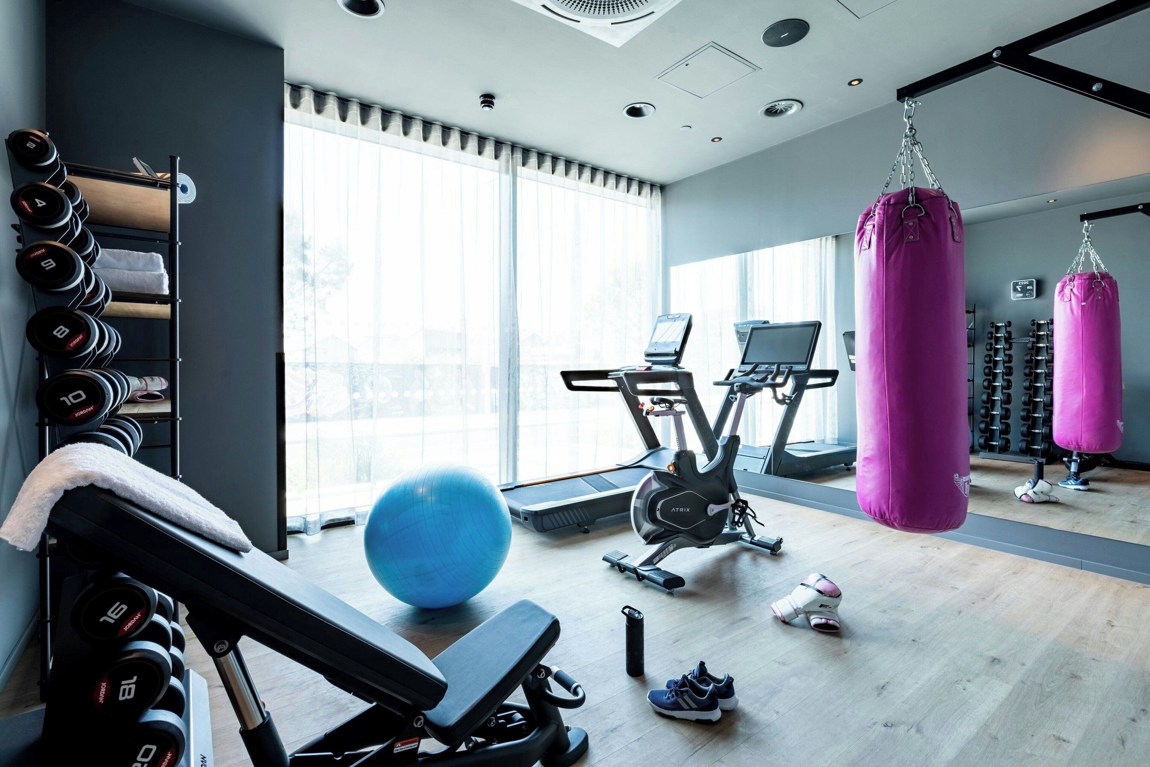 A gym with exercise equipment, a punching bag, and a large window providing natural light.
