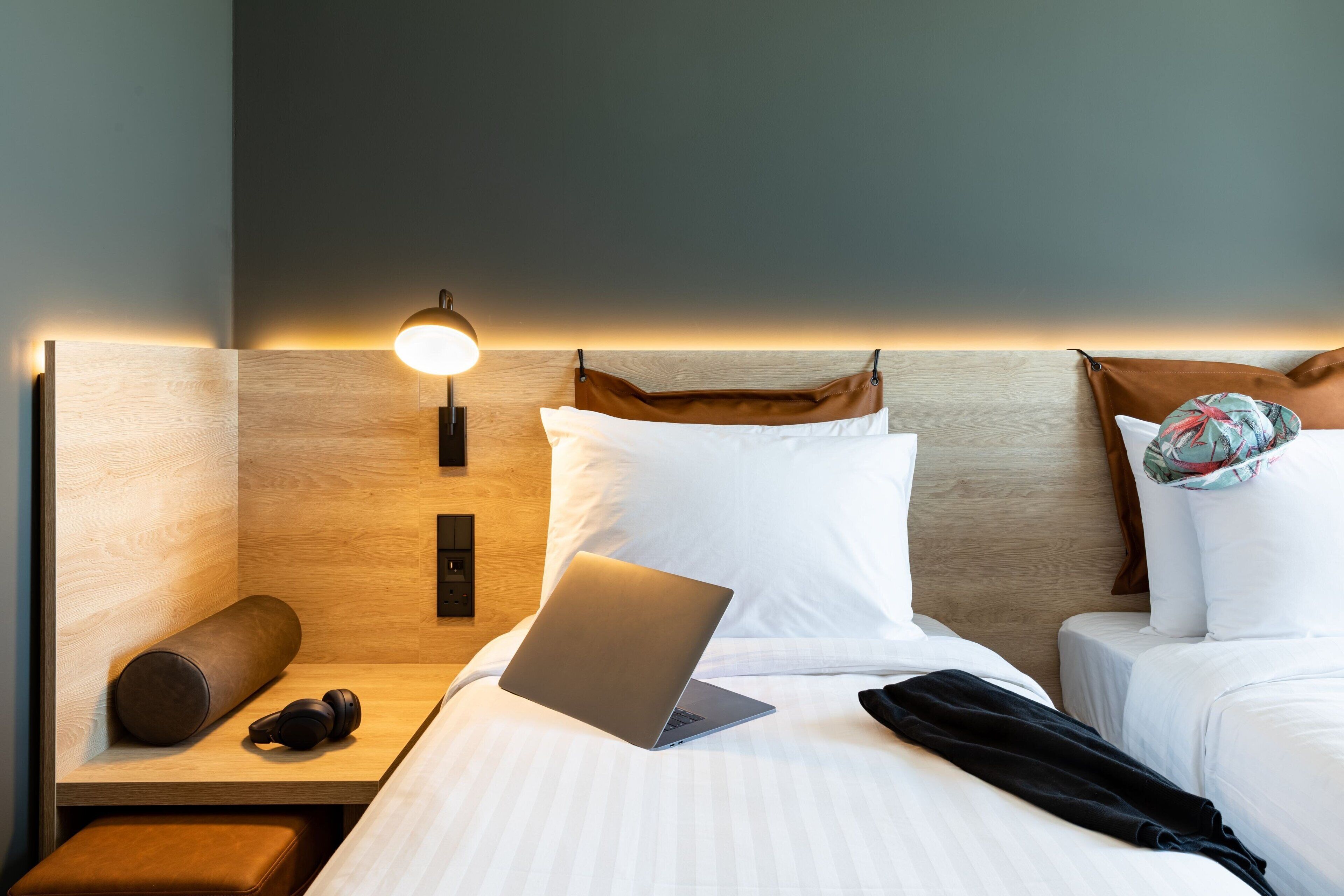 Et hotelværelse med seng, bærbar computer, pude, lampe og et natbord.