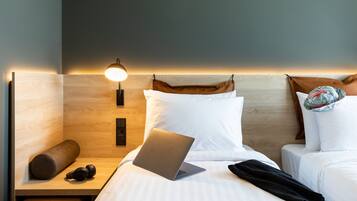 A hotel room with a bed, a laptop, a pillow, a lamp, and a bedside table.