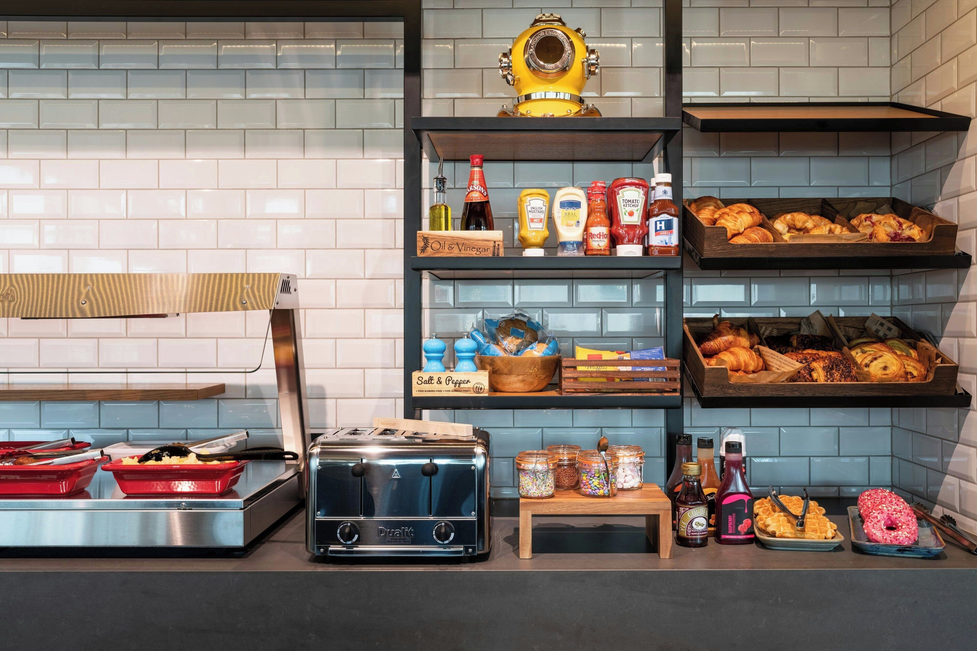 A kitchen with a toaster, shelves with condiments, and a tray of pastries.