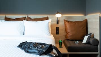 A neatly made bed with pillows, a leather jacket, a green tumbler, and a tablet on a bedside table.