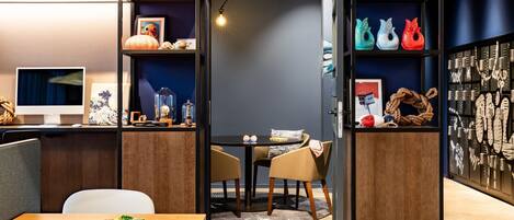 Una habitación moderna con un escritorio de madera, una computadora portátil y una tableta. Se observan estanterías con objetos decorativos y una pared con fotografías enmarcadas.