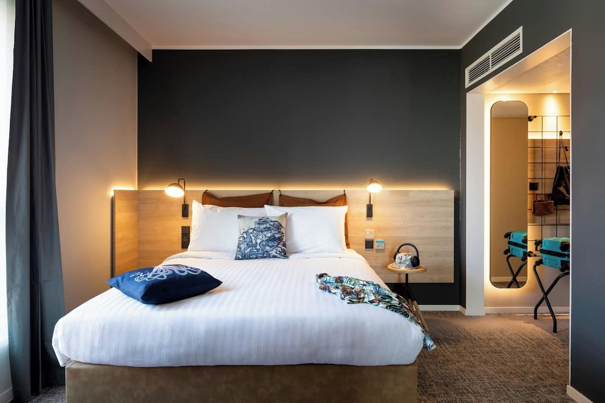A modern hotel room with a large bed, bedside tables, a mirror, and a view of the hallway.