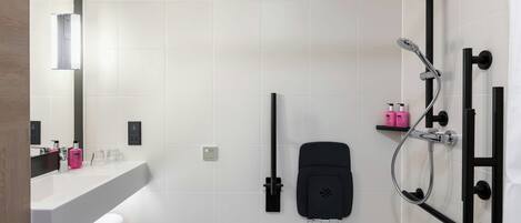 Un baño moderno con un lavamanos grande de color blanco, un perchero negro, un cabezal de ducha de mano y un dispensador de jabón negro.