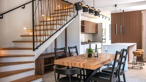 Une cuisine moderne avec des meubles en bois, une table à manger avec des chaises et un escalier avec des rampes noires.