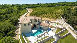 Une maison à deux étages avec une piscine, entourée d’un vignoble et bordée d’un chemin en pierre.