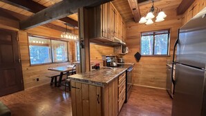 Eine Holzhütte mit einer Küche, die eine zentrale Kochinsel, Holzausstattung, einen Edelstahlkühlschrank und einen Essbereich mit Tisch und Stühlen beinhaltet.