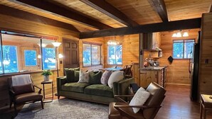 Ein gemütliches Holzblockhaus mit einem grünen Sofa, Sesseln und einem Essbereich.