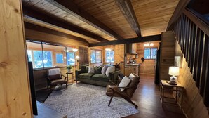 Ein gemütliches Blockhaus-Interieur mit Holzbalkendecke, einem grünen Sofa, einem Holzesstisch und einer Küchenzeile.
