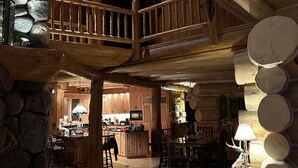 Un intérieur spacieux de chalet en bois, avec un plafond haut, des poutres apparentes, un mur en pierre et une cheminée chaleureuse.