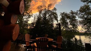 Une terrasse en bois avec des sièges extérieurs et une vue sur un lac au coucher du soleil.