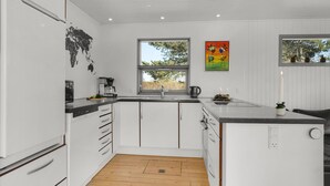 Una cucina moderna con mobili bianchi, un piano di lavoro nero, una macchina per caffè e una finestra con vista sugli alberi.