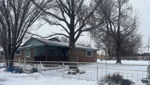 Una casa con fachada de ladrillo y tejado azul, rodeada por un patio cubierto de nieve y una valla de metal.
