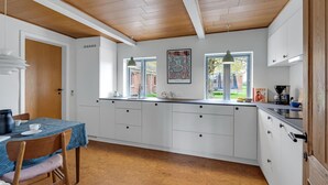 Une cuisine moderne avec des meubles blancs, un plafond en bois et un coin repas comprenant une table et des chaises.
