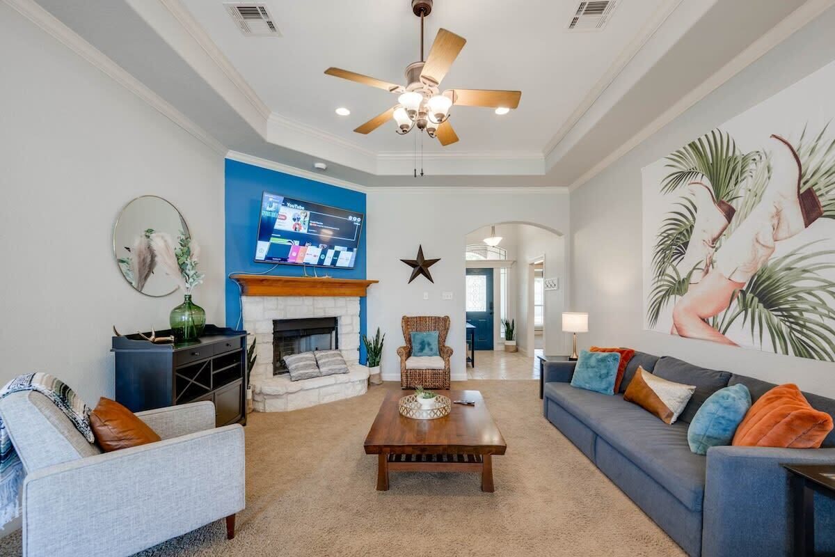 A spacious living room with a fireplace, a ceiling fan, and a large wall-mounted TV.