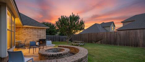 A backyard with a brick fire pit, outdoor seating, and a wooden fence.