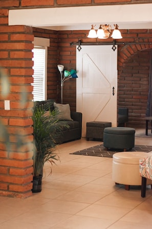 A living room with a brick wall, a sofa, a coffee table, and a door with a decorative handle. - Campanario San Emilion (Baja)